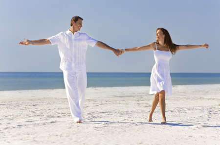 Happy romantic man and woman couple dancing and holding hands on a deserted tropical beach with bright clear blue skyの写真素材