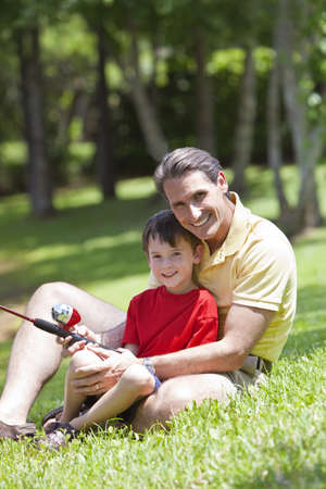 A father teaching his son how to fish on a river outside in summer sunshineの写真素材