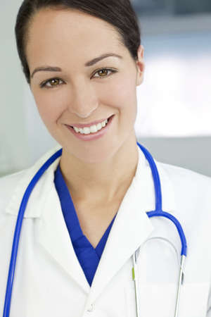 An attractive smiling female doctor wearing a white coat and stethoscope in a hospital.の写真素材