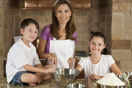 An smiling mother, daughter and son family cooking and baking chocolate chip cookies in a kitchen at homeの写真素材