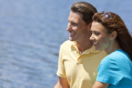 Portrait shot of an attractive, successful and happy middle aged man and woman couple in their thirties, sitting together outside smiling with a natural water background.の写真素材