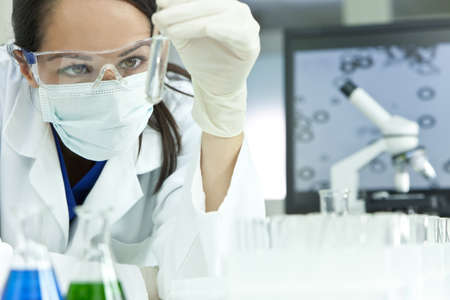 A female medical or scientific researcher or woman doctor looking at a test tube of clear solution in a laboratory with her microscope beside her.の写真素材