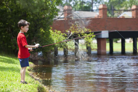 A young boy fishing on a river outside in summer sunshineの写真素材