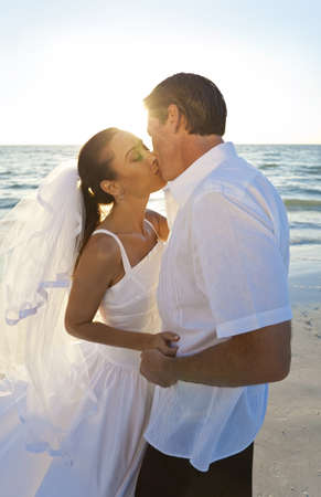 Married couple, bride and groom, kissing at sunset on a beautiful tropical beach weddingの写真素材