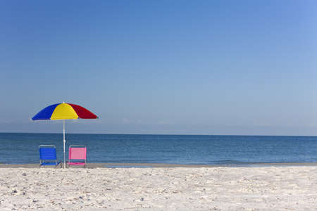 Pink and blue deck chairs on a beach underneath a colourful umbrella or parasolの写真素材