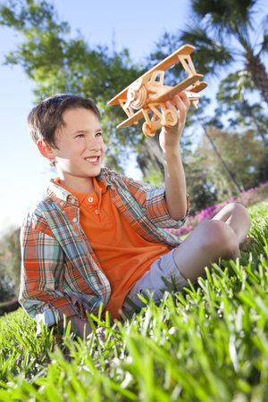 A young boy outside sitting on the grass playing with his toy model airplaneの写真素材