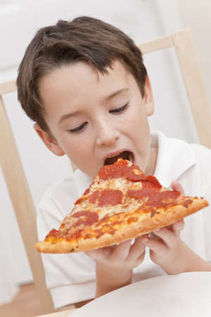 A young boy child eating a slice of pepperoni and cheese pizzaの写真素材