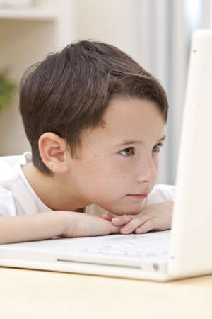 A young boy child resting on his hands and looking at the screen while using laptop computerの写真素材