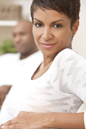 A happy African American man and woman couple in their thirties sitting at home, the woman is in focus in the foreground the man out of focus in the background.の写真素材