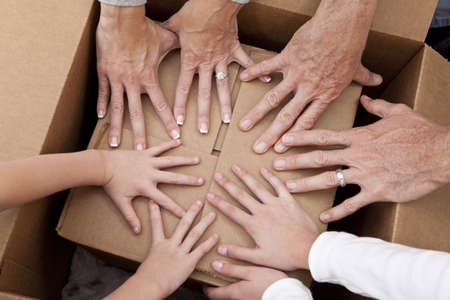Concept photograph of family hands, parents son and daughter, unpacking a box and moving into a new home.の写真素材