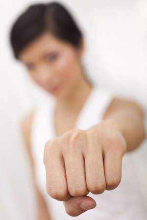 A beautiful Chinese Asian Oriental girl performing a martial arts fist punch to the camera, the focus is on her fistの写真素材