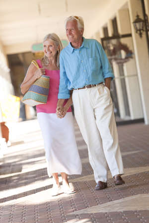 Happy senior man and woman couple holding hands and walking through a sunlit shopping mallの写真素材