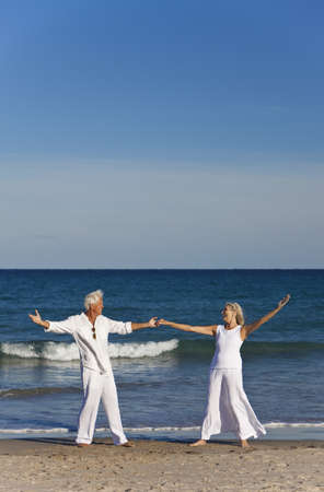 Happy senior man and woman couple dancing and holding hands on a deserted tropical beach with bright clear blue skyの写真素材