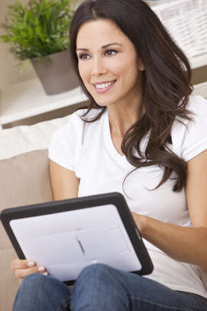 Beautiful young brunette woman at home sitting on sofa or using her tabletの写真素材