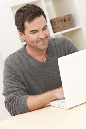 Smiling man in his thirties at home using his laptop computerの写真素材