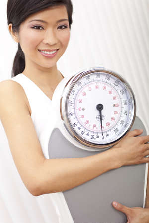 Happy & beautiful Oriental Asian Chinese woman holding weighing scales at gym or health clubの写真素材