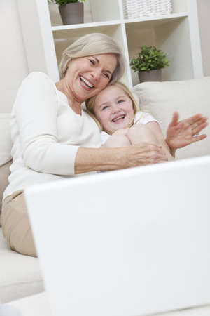 A senior woman grandmother and her young child grand daughter laughing and having fun at home with a laptop computerの写真素材