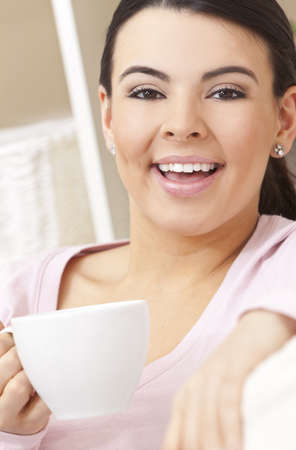A beautiful young Latina Hispanic woman or girl with a wonderful enigmatic smile drinking tea or coffee from a white cup の写真素材