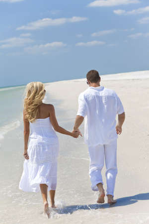 Happy young man and woman couple running or walking and holding hands on a deserted tropical beach with bright clear blue skyの写真素材