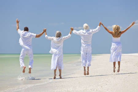 Rear view of four people, two seniors, couples or family generations, holding hands, having fun and jumping in celebration on a tropical beachの写真素材