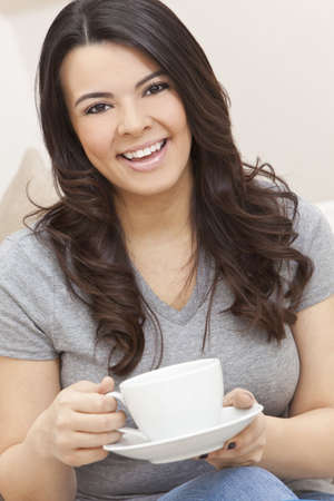 A beautiful young Latina Hispanic woman or girl with a wonderful enigmatic smile drinking tea or coffee from a white cupの写真素材