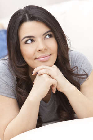 Portrait of a beautiful young Latina Hispanic woman laying on a sofa at home relaxing and smiling の写真素材