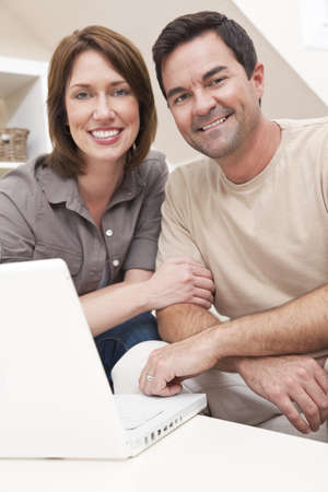 Happy man and woman couple in their thirties, sitting together at home on a sofa using a laptop computerの写真素材