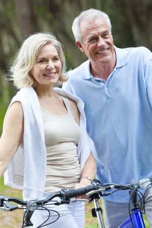 Happy senior man and woman couple sitting together smiling and happy with bicycles at a parkの写真素材
