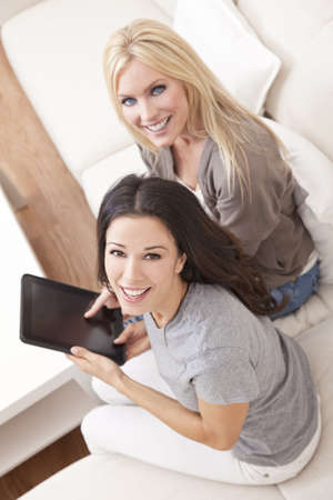 Overhead photograph of two beautiful young women at home sitting on sofa or settee using a tablet PC computer and smilingの写真素材