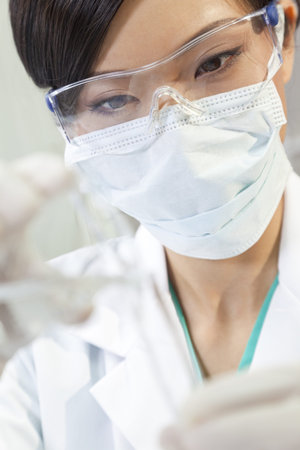 A Chinese Asian female medical or scientific researcher or doctor using looking at a test tube of...