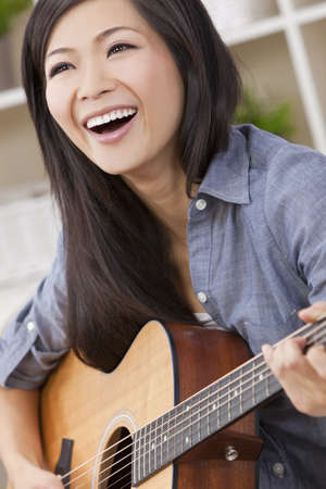 A beautiful happy young Chinese Asian Oriental woman with a wonderful toothy smile holding her guitar の写真素材