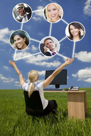 Business or social network connections concept photograph of woman businesswoman sitting at a desk using a computer in a green field raising her arms into a bright blue sky with fluffy white clouds の写真素材