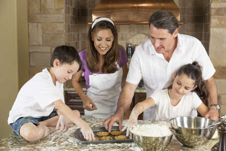 An attractive smiling family of mother, father, and two children baking and eating fresh chocolate chip cookies in a kitchen at homeの写真素材