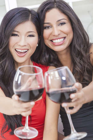 Two beautiful young women friends, Asian Chinese and Hispanic having fun drinking red wine togetherの写真素材