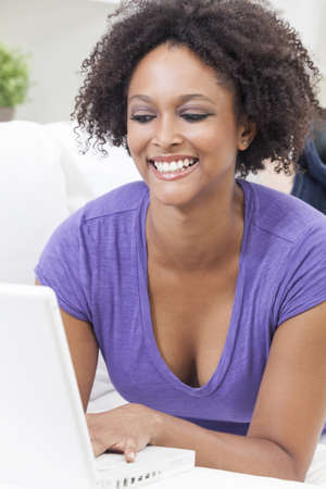 A beautiful happy mixed race African American girl or young woman laying down on sofa using a laptop computerの写真素材