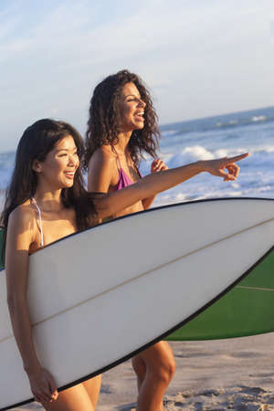 Beautiful young women surfer girls in bikinis with surfboards on a beach at sunset or sunriseの写真素材
