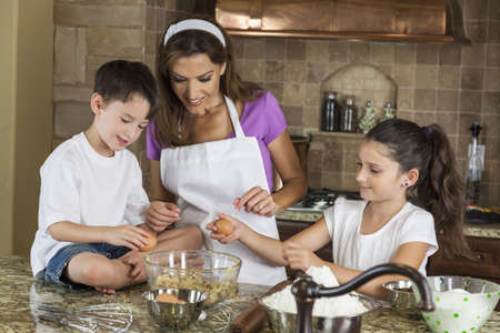An attractive smiling family of mother, two children, girl, boy, son & daughter, breaking eggs & baking in a kitchen at homeの写真素材