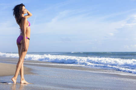A sexy young brunette woman or girl wearing a purple bikini on a deserted tropical beach with a blue sky の写真素材