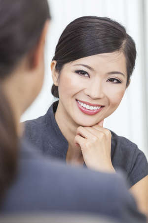 Portrait of a beautiful young Asian Chinese woman or businesswoman in office meeting with female colleagueの写真素材