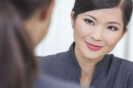 Portrait of a beautiful young Asian Chinese woman or businesswoman in office meeting with female colleagueの写真素材