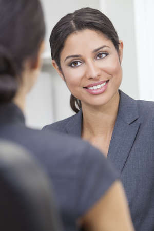 Beautiful young Latina Hispanic woman or businesswoman in smart business suit sitting at a desk in an office having a meeting with colleagueの写真素材