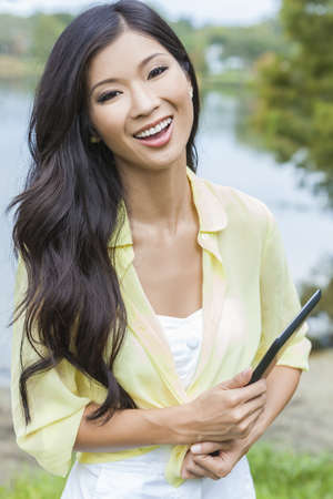 Happy, smiling, beautiful Asian Chinese young woman or girl student outside holding tablet computerの写真素材
