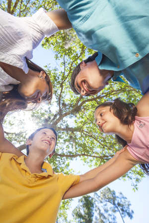 An attractive happy, smiling family of mother, father, son and daughter hugging in a huddle together outside in a park enjoying warm summer sunshineの写真素材