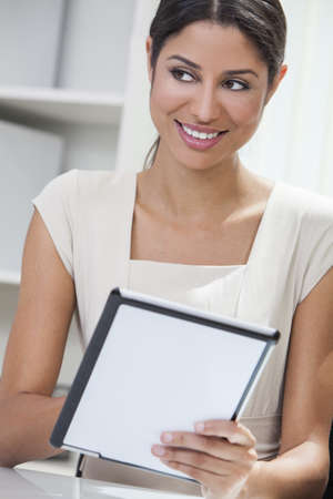 Beautiful young Latina Hispanic woman or businesswoman in an office and using a tablet computerの写真素材