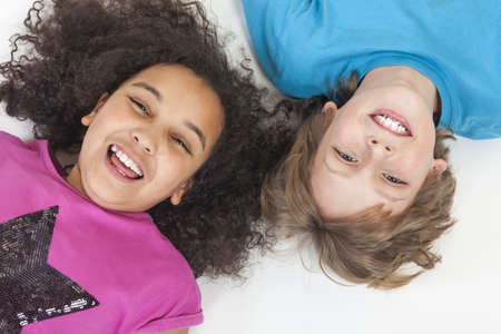Overhead photograph of two children, blond boy and mixed race African American girl, having fun laying down and laughingの写真素材