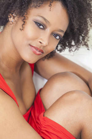 A beautiful sexy mixed race African American girl or young woman wearing a red dress looking happy and smilingの写真素材