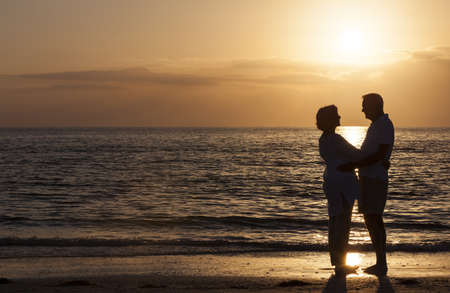 Happy senior man and woman couple together hugging embracing at sunset on a deserted tropical beach の写真素材