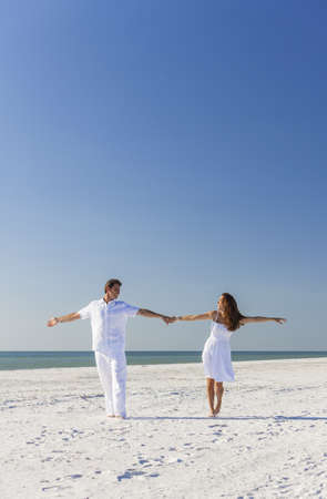 Middle aged happy man and woman romantic couple in white clothes dancing on a deserted tropical beach with bright clear blue skyの写真素材
