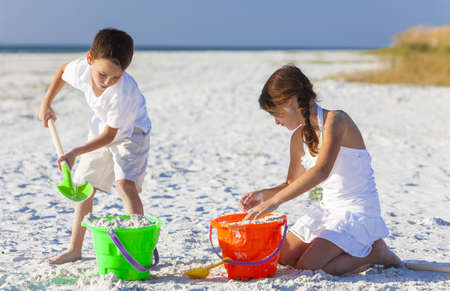 Happy children, boy & girl, brother& sister having fun playing in the sand on a beach with bucket and spadeの写真素材