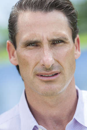 An outdoor portrait of handsome middle aged man shot with sunlight against a natural blue and green backgroundの写真素材
